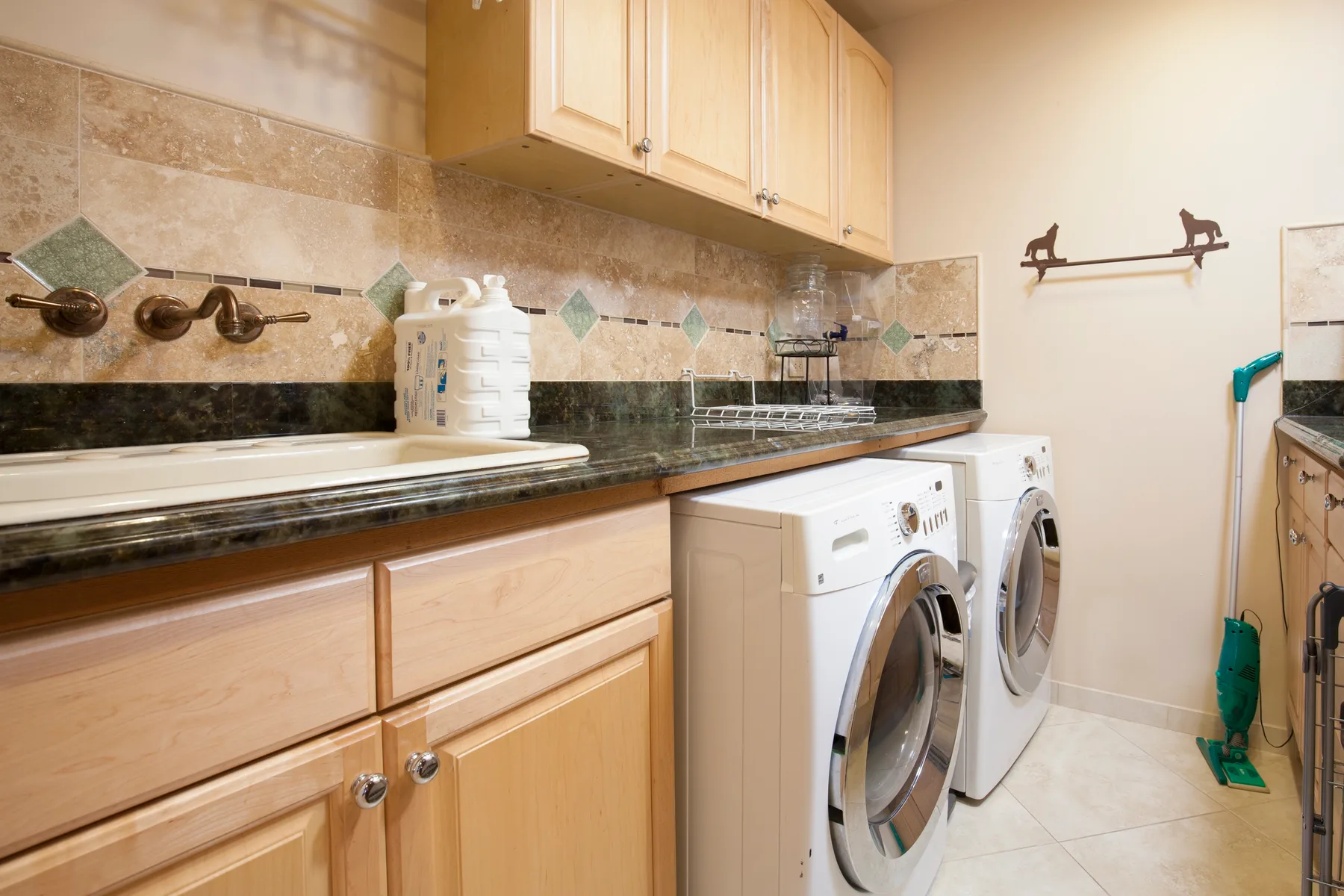 A laundry room with front-loading machines beneath a counter and cabinets.