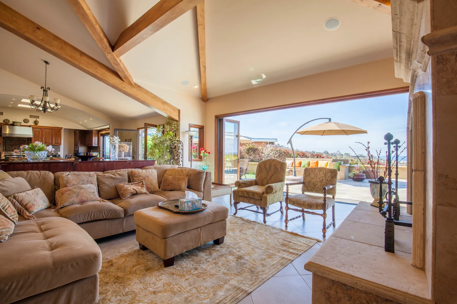 A bright living room opens onto a patio, with exposed wooden beams overhead.