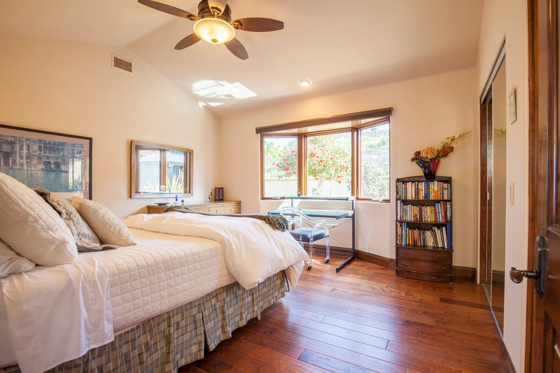 A bright bedroom with beds, a large window, and a bookcase.