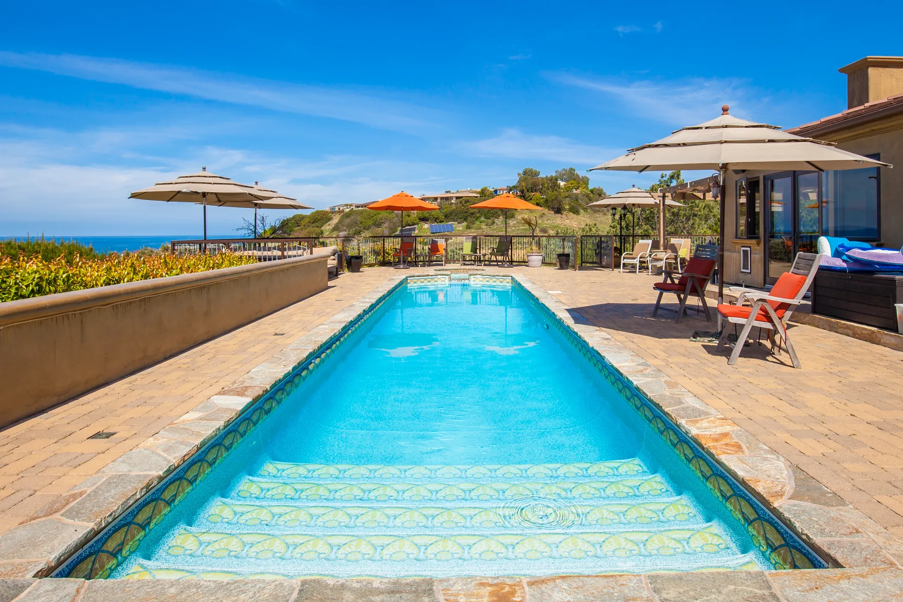 An outdoor swimming pool sits on a sunny terrace with lounge chairs and umbrellas.