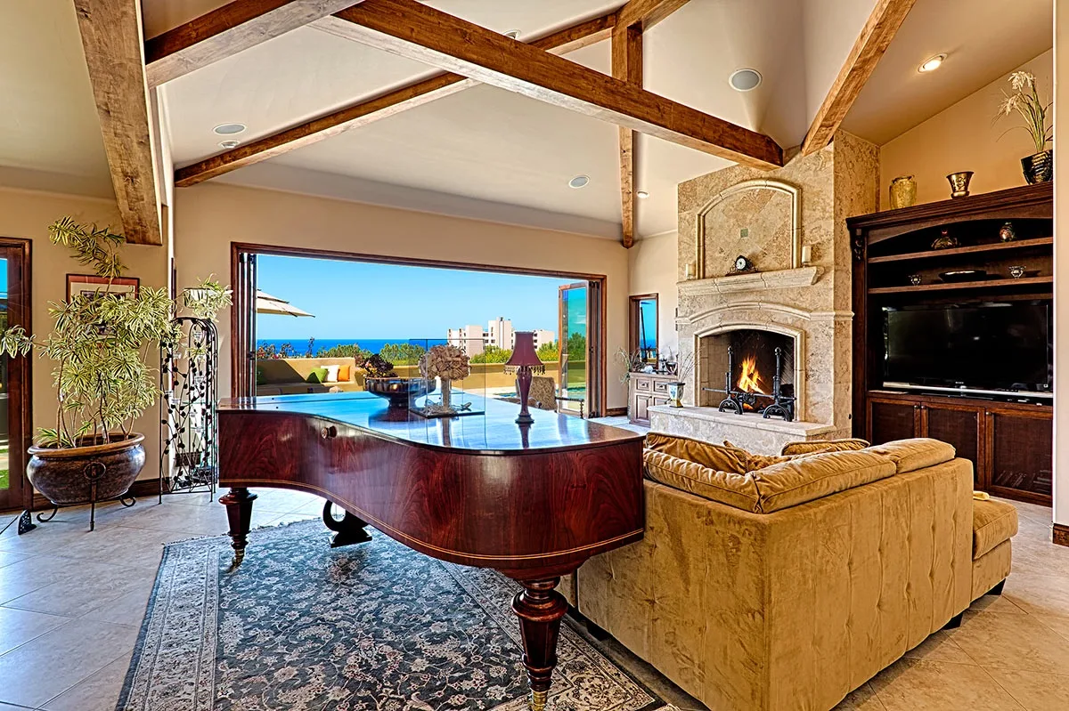 A living room with a grand piano, seating, and an ocean view through open doors.