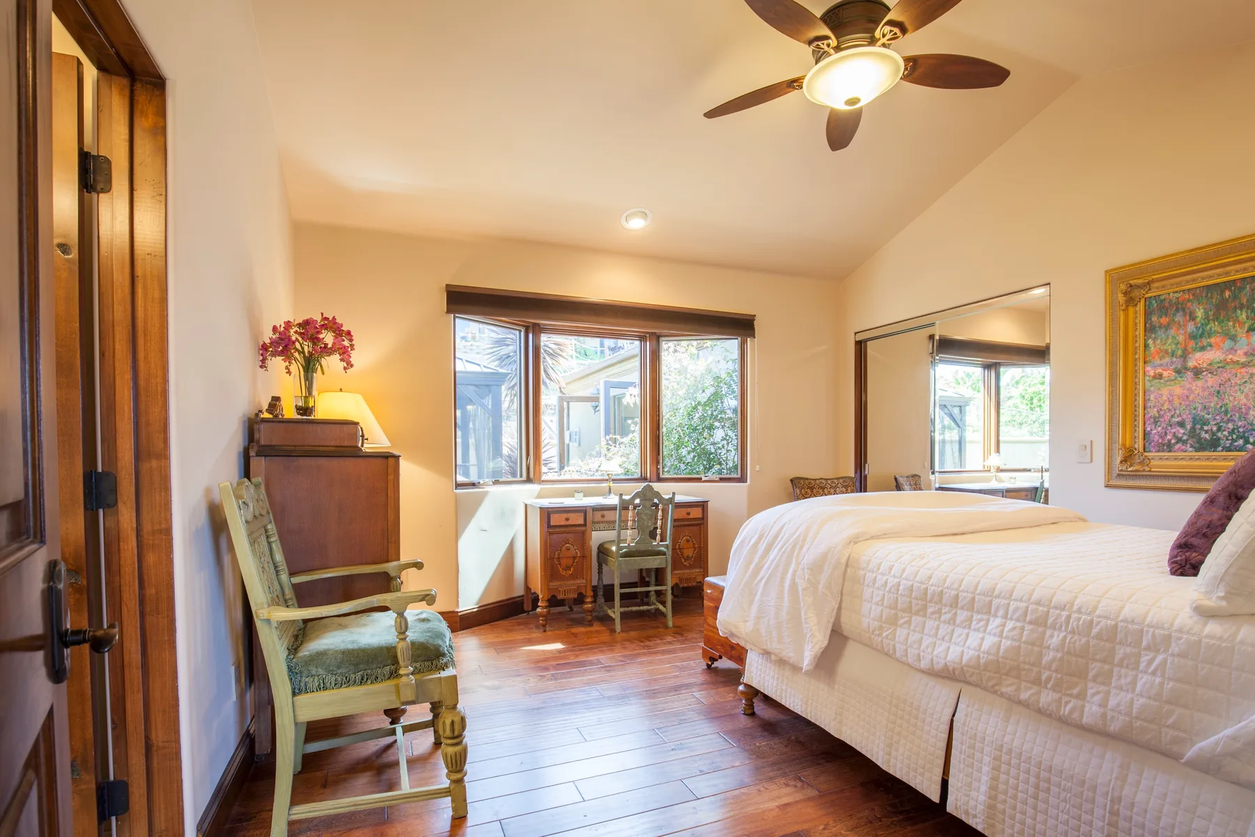 A bedroom with a bed, a desk by the window, and a ceiling fan.