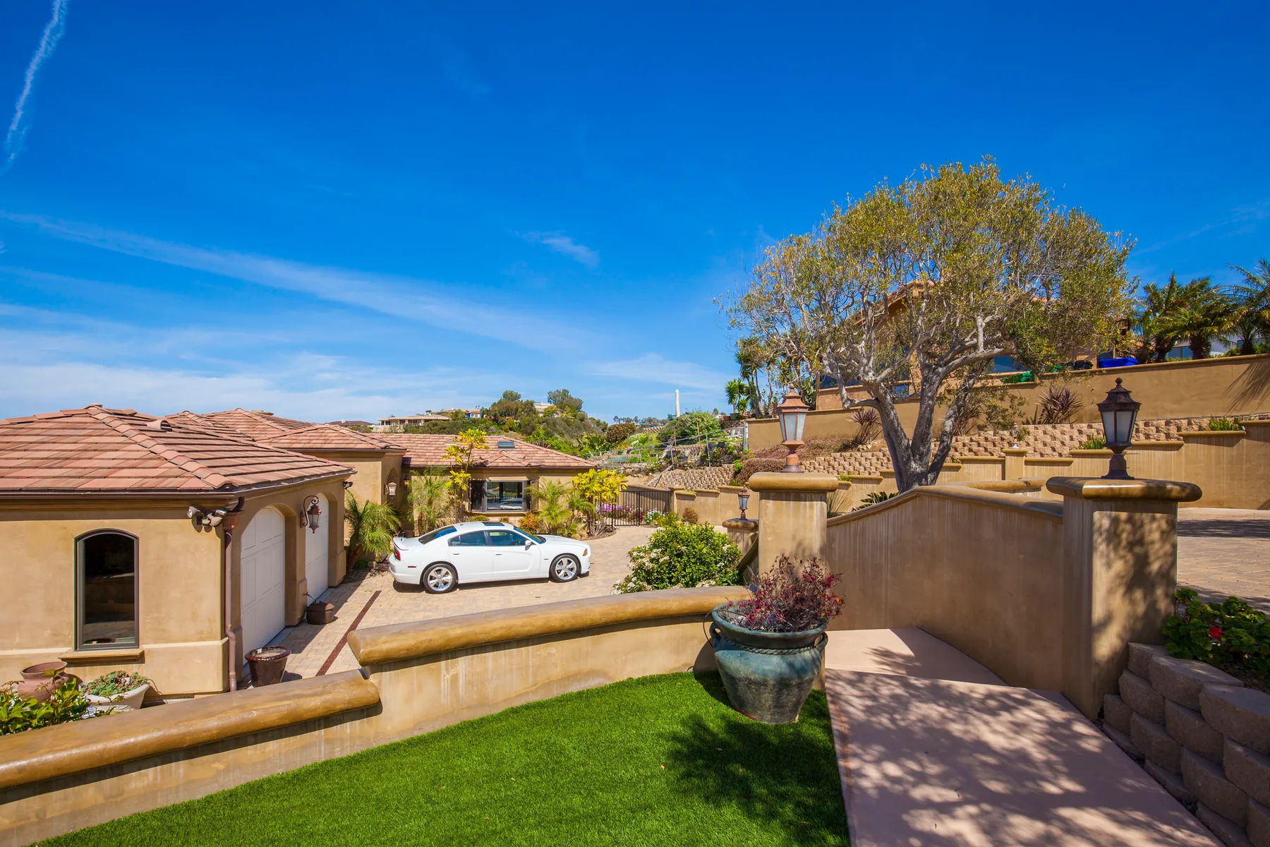 A sunny courtyard with a paved walkway, green lawn, and a parked car.