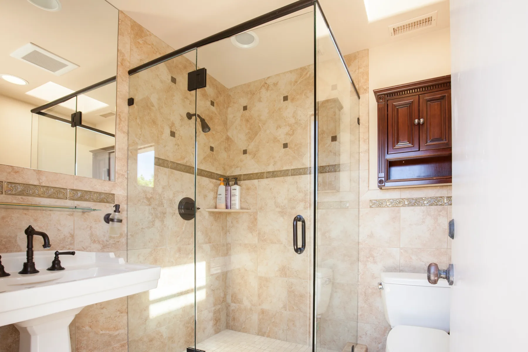 A tiled bathroom with a glass shower, sink, and toilet.
