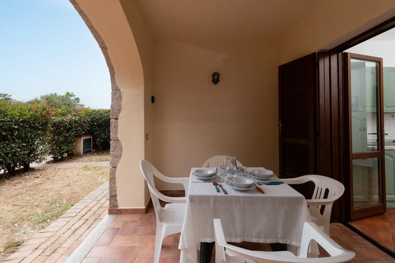 Un patio cubierto con una mesa y sillas junto a unas puertas abiertas.