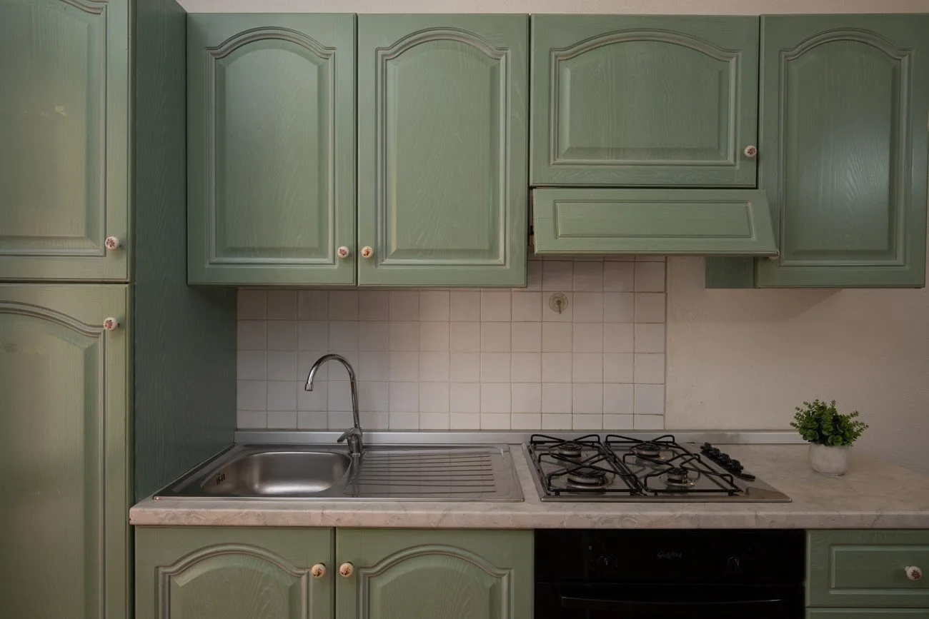 Una cocina con gabinetes verdes, fregadero y estufa de gas.