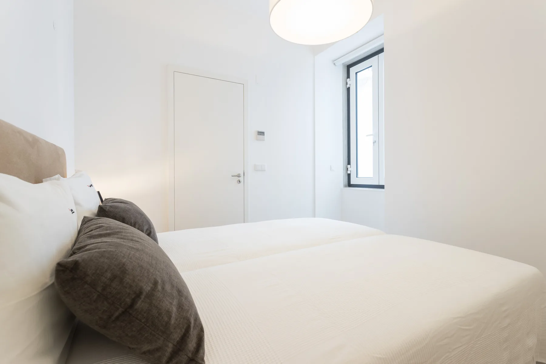 Un dormitorio luminoso con una cama, ropa de cama neutra y una ventana.