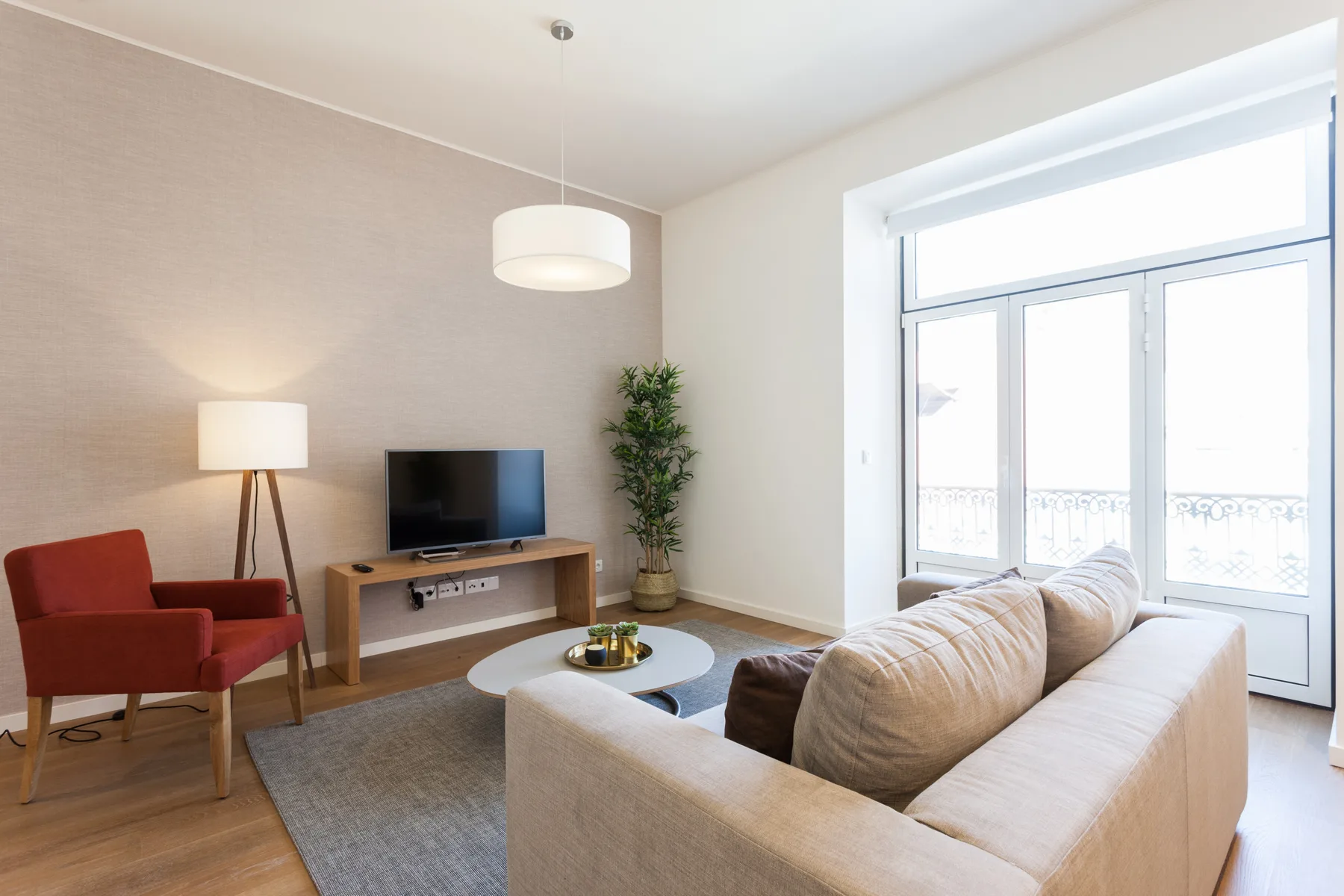 Una sala luminosa con asientos, un televisor y grandes ventanales.