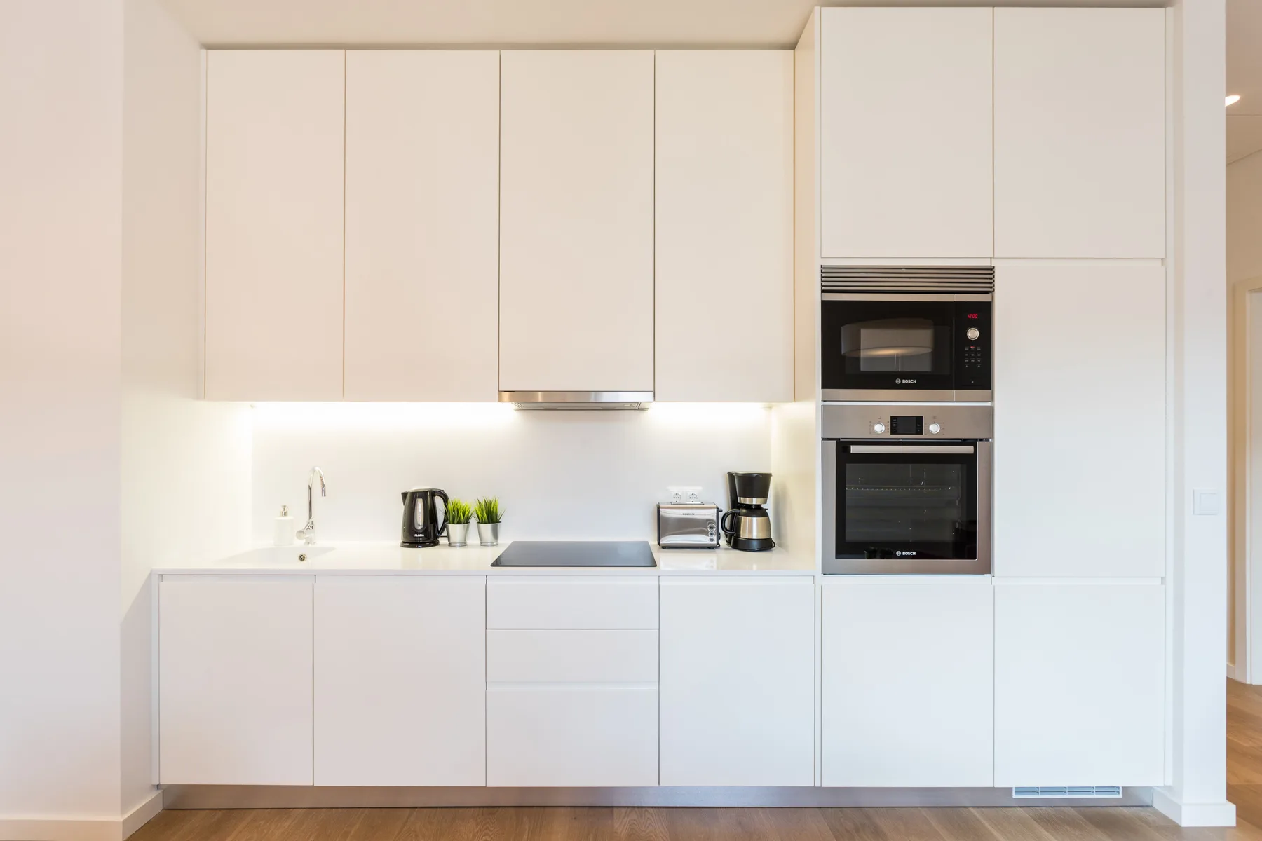 Una cocina moderna y luminosa con armarios blancos y electrodomésticos integrados.