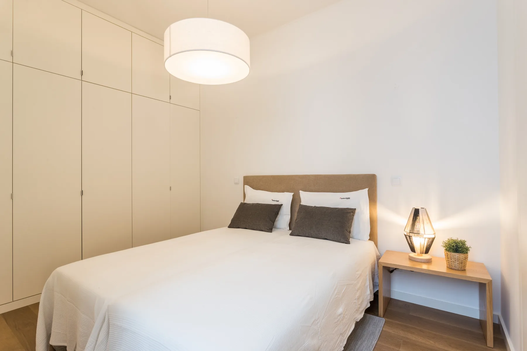 A bedroom with a neatly made bed and a bedside table.