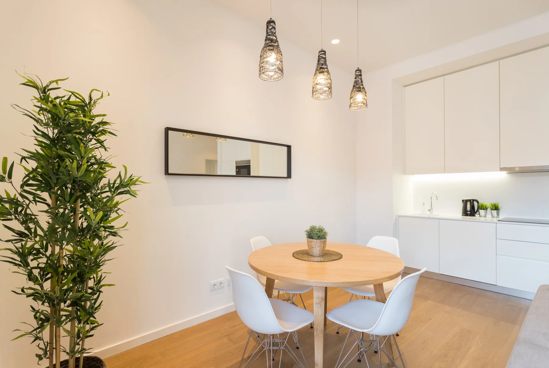 Comedor con una mesa redonda y asientos blancos junto a una cocina luminosa.
