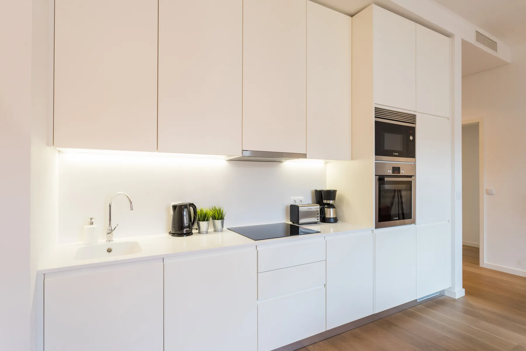 Una cocina moderna y luminosa con armarios blancos y electrodomésticos integrados.