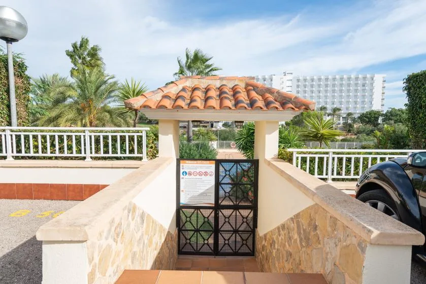 A tiled-roof entrance with a metal gate opens onto a palm-lined path.