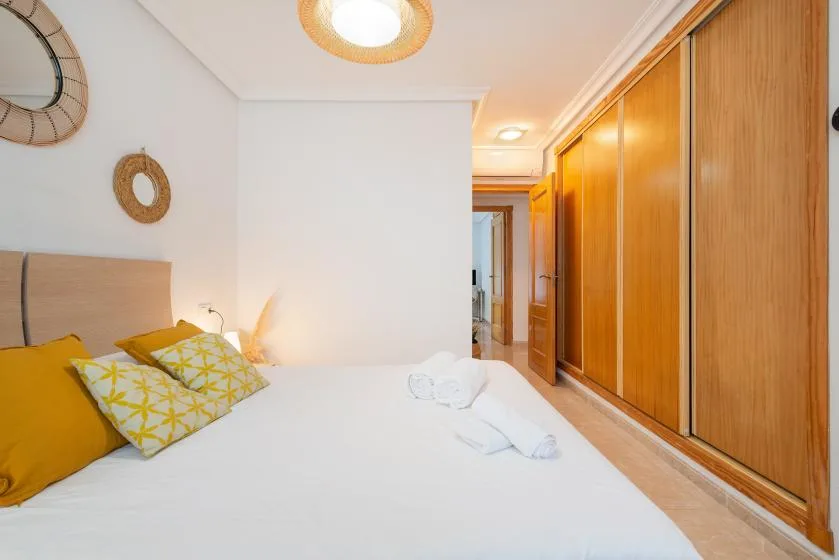 A bedroom with a white bed, yellow pillows, and wooden wardrobes.