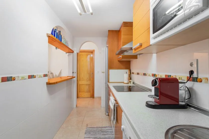 A narrow kitchen with wooden cabinets, a countertop, and a coffee machine.