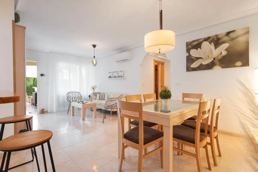 A bright dining area with a wooden table, chairs, and a large floral wall picture.