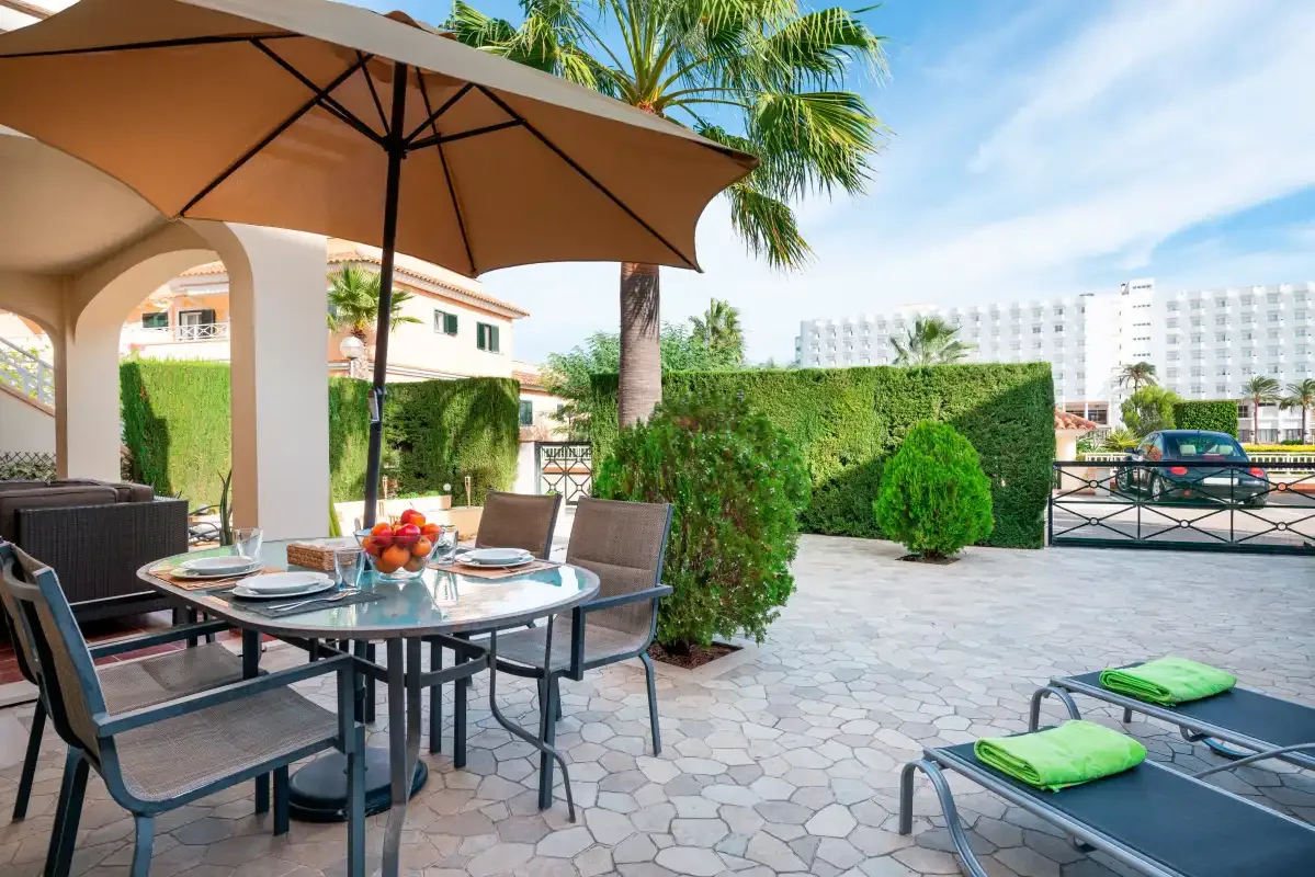 A paved outdoor patio has a dining table under a large umbrella.