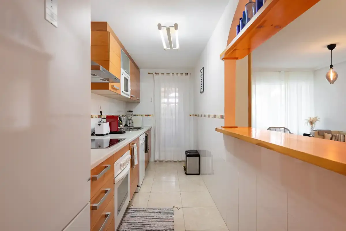 A narrow kitchen with wooden cabinets and a counter opening into a dining area.