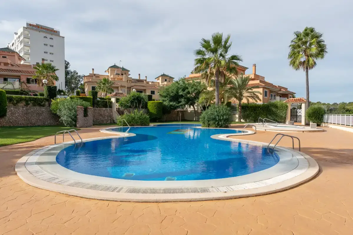 A swimming pool sits among landscaped grounds and palm trees.