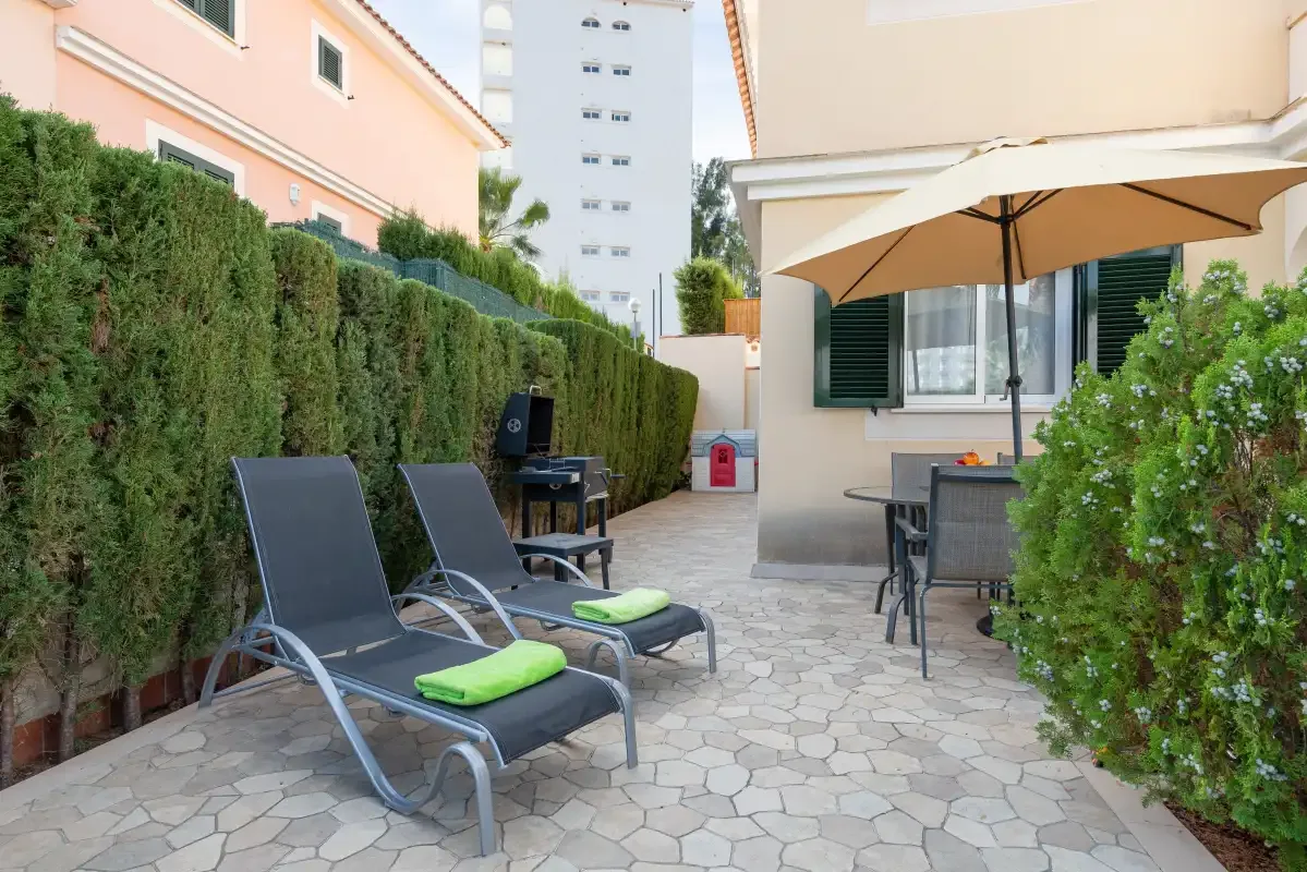 A paved outdoor patio with reclining seating and a large shade umbrella.