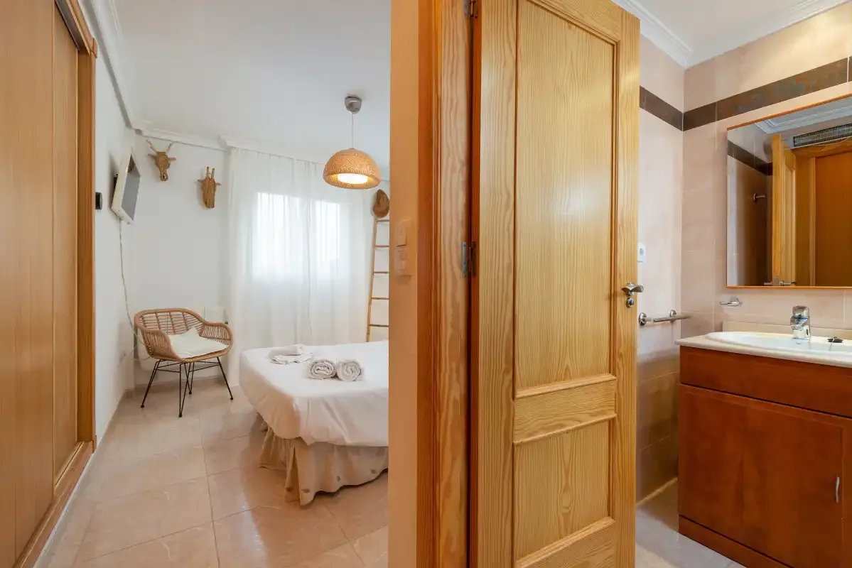 A bedroom with a bed and chair is visible beyond the bathroom doorway.