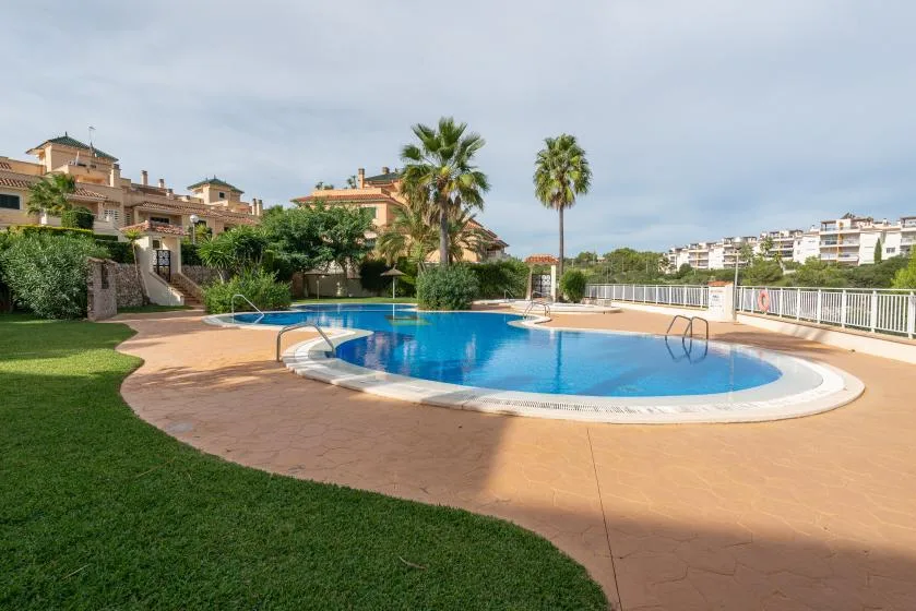 Outdoor swimming pool surrounded by a paved deck, lawn, and palm trees.