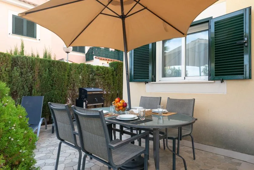 An outdoor dining area sits beneath a large patio umbrella beside a hedge.