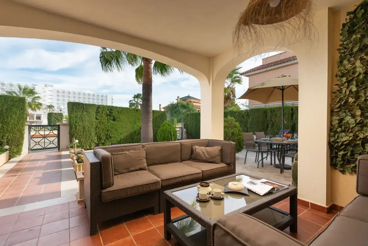 A covered patio has outdoor seating and a dining area beside the garden.