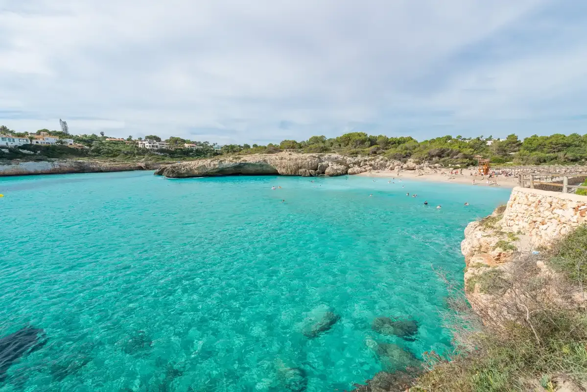 A turquoise swimming cove is bordered by rocky shores under a cloudy sky.
