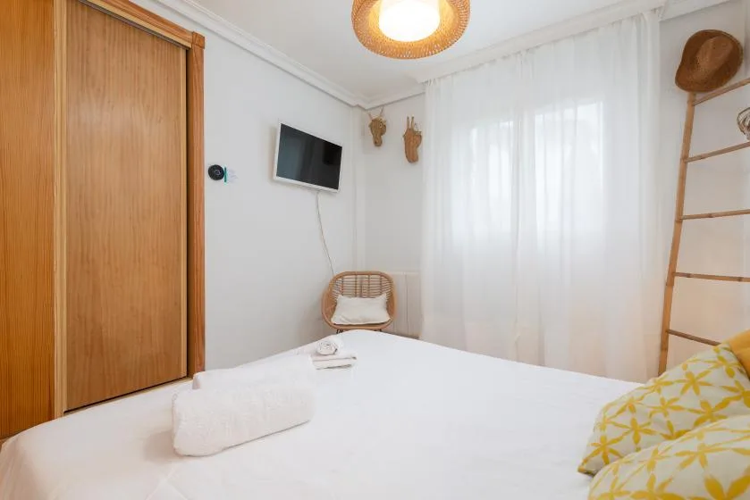A bright bedroom with a white bed, sheer curtains, and a wall-mounted television.