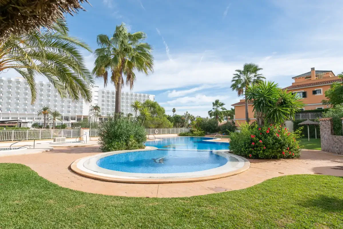 An outdoor swimming pool sits among palm trees and landscaped greenery.