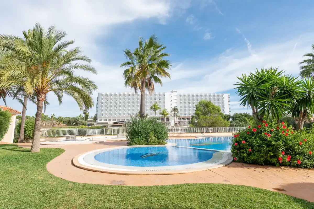 An outdoor swimming pool sits among palm trees and landscaped greenery.