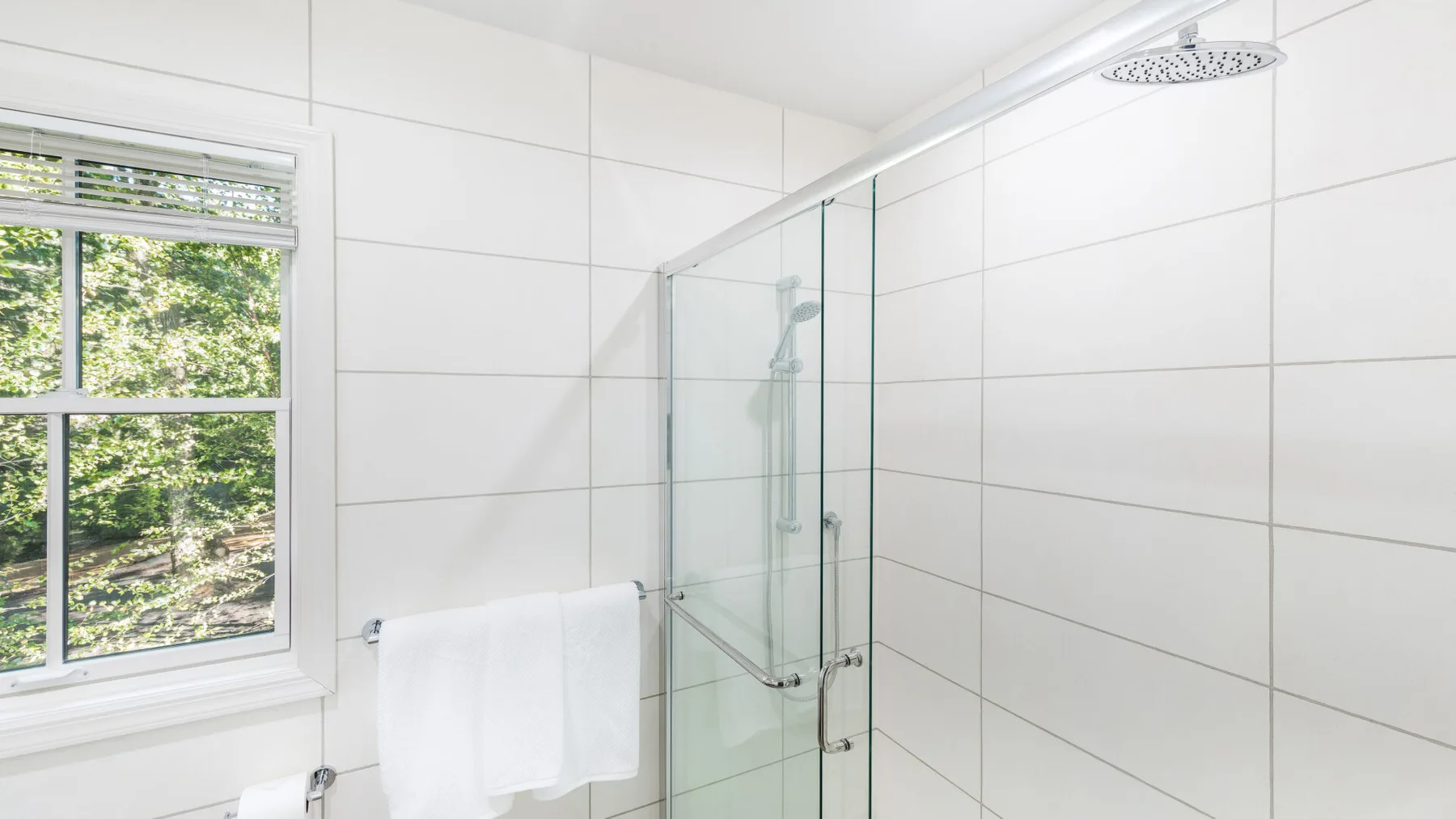 Un baño luminoso con una ducha de vidrio y una ventana con vista al follaje.