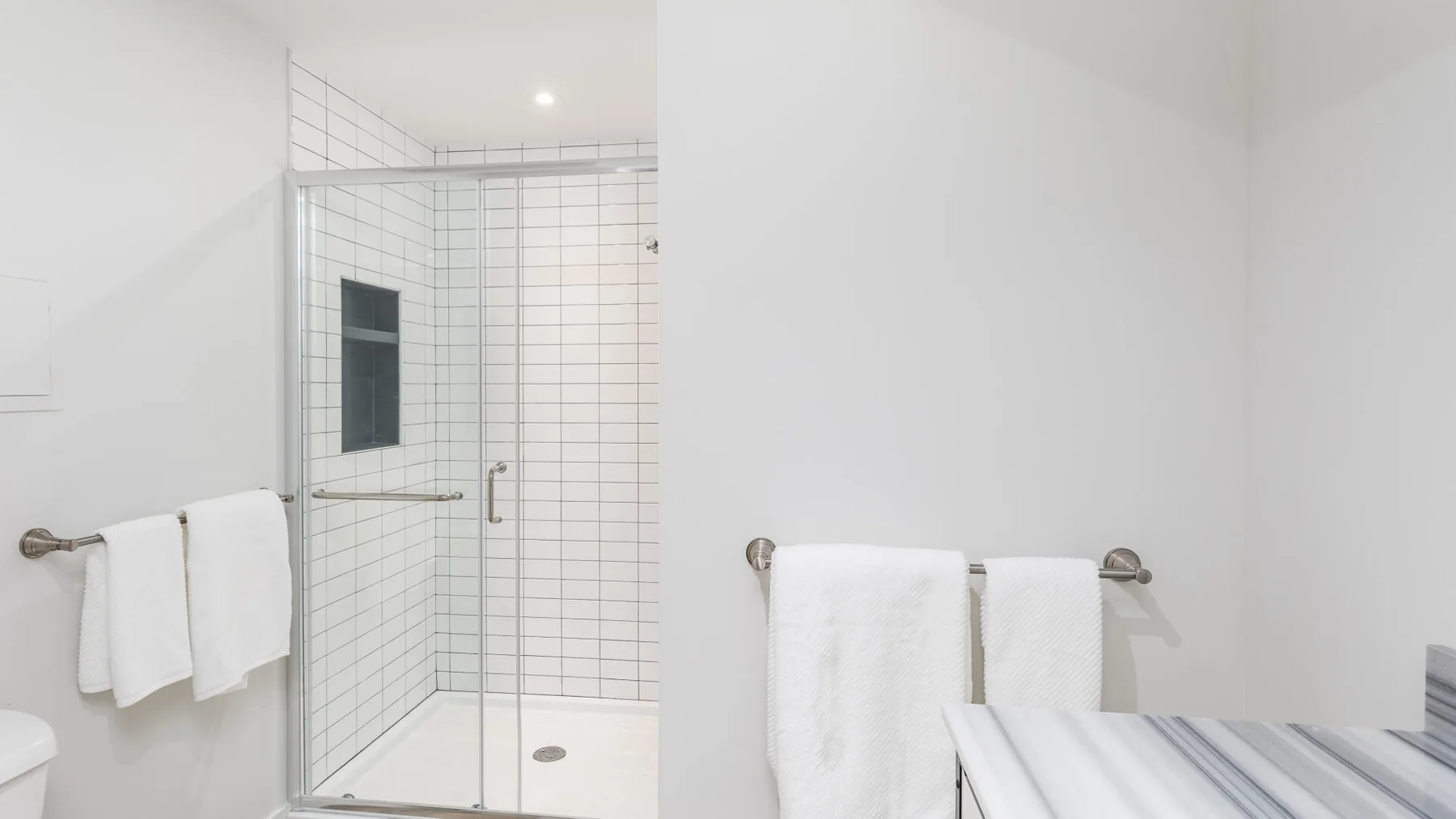 Un baño luminoso con una ducha de vidrio y toallas blancas colgadas cerca.