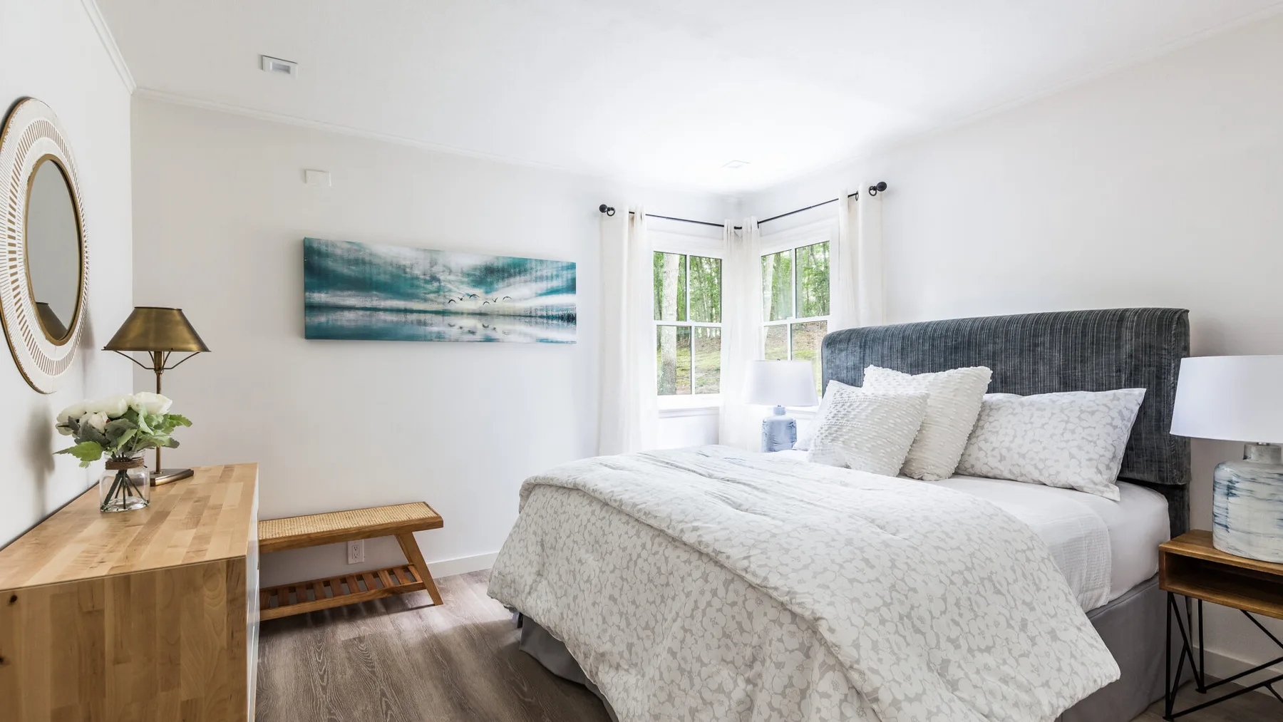 Un dormitorio luminoso con una cama, una cómoda de madera y ventanas.