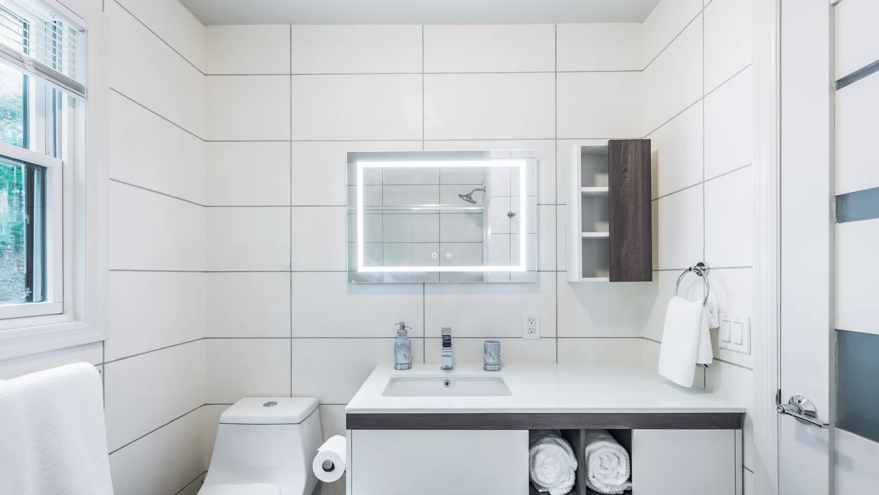 Un baño luminoso con azulejos, lavabo, espejo e inodoro.