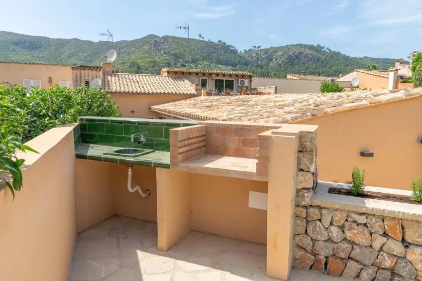 Una terraza en la azotea con una encimera de azulejos y un fregadero de vidrio verde mira hacia las colinas.