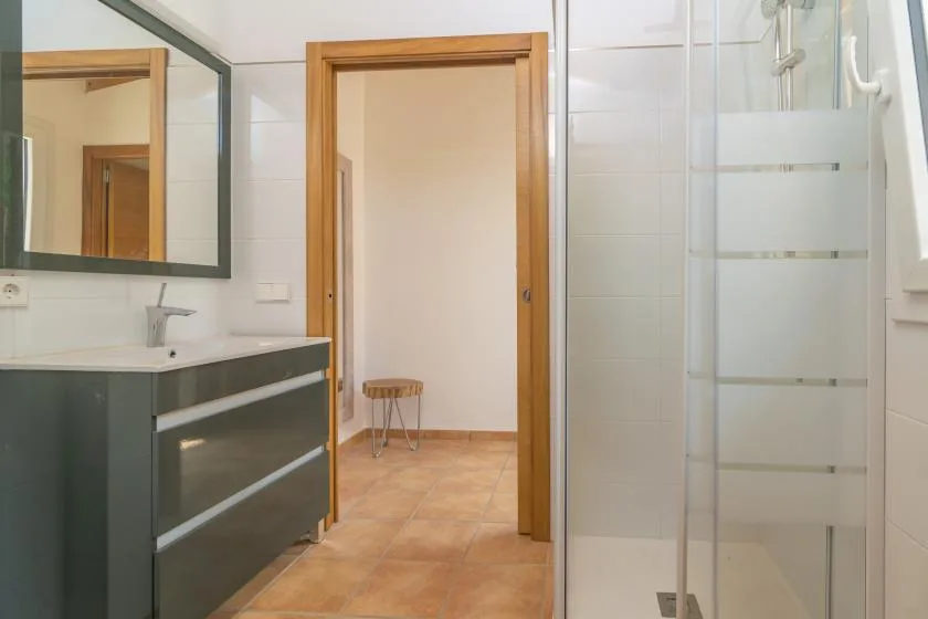 Un baño con lavabo, espejo y ducha de vidrio junto a una puerta abierta.