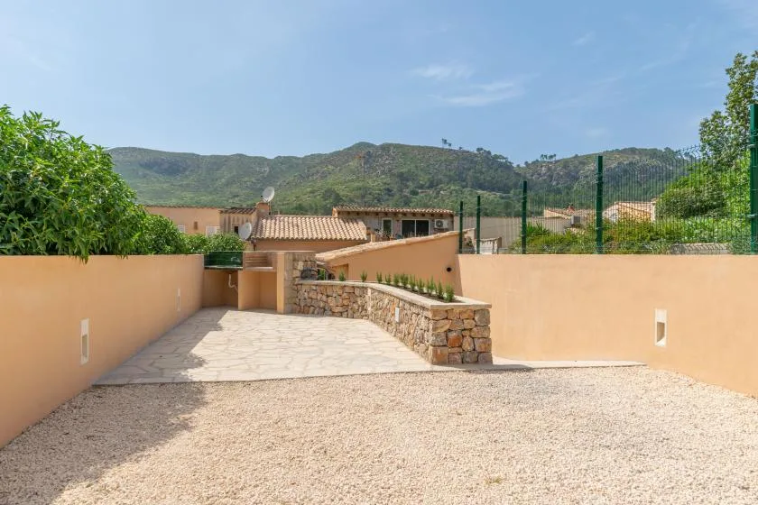 Un patio exterior con un camino pavimentado, grava y jardineras bajas de piedra.