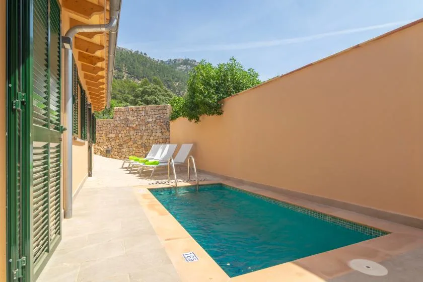 Una piscina exterior estrecha junto a un edificio, con asientos junto al borde pavimentado.