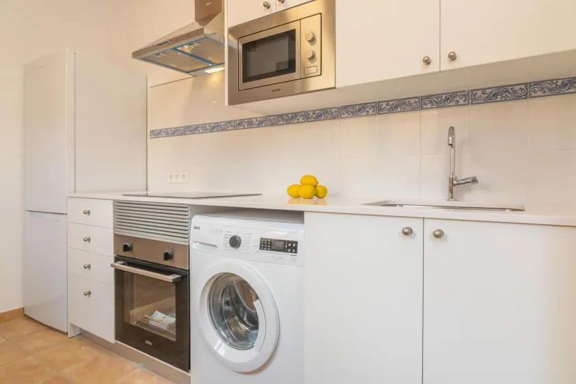 Una cocina luminosa con armarios blancos, una lavadora y limones sobre la encimera.