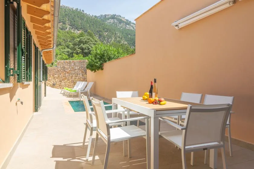 Una zona de comedor al aire libre con mesa y asientos junto a una pequeña piscina.