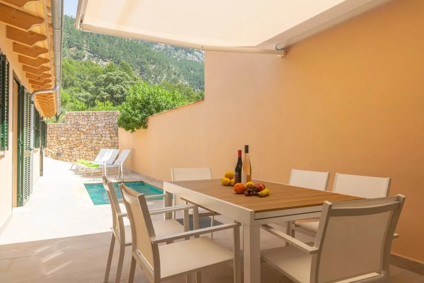 A covered outdoor dining area with a table and seating beside a small pool.