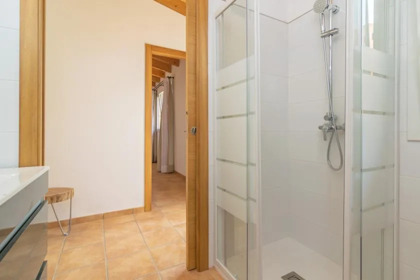 Un baño con suelo de baldosas, ducha de vidrio y una puerta a otra habitación.