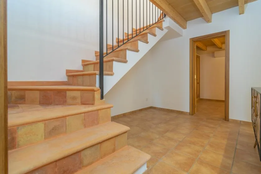 Un recibidor interior con suelo de baldosas, una escalera de madera y una puerta abierta.