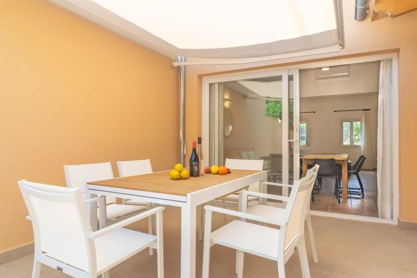 A dining area with a table and white seating opens into another room.