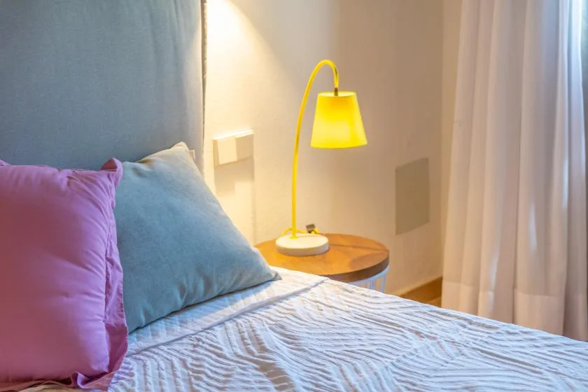 Un dormitorio con cojines de colores, una mesita de noche y una lámpara amarilla.