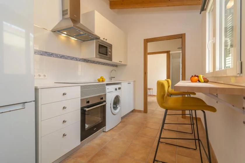 Una cocina luminosa con zona de cocción, lavadora y barra para desayunar.