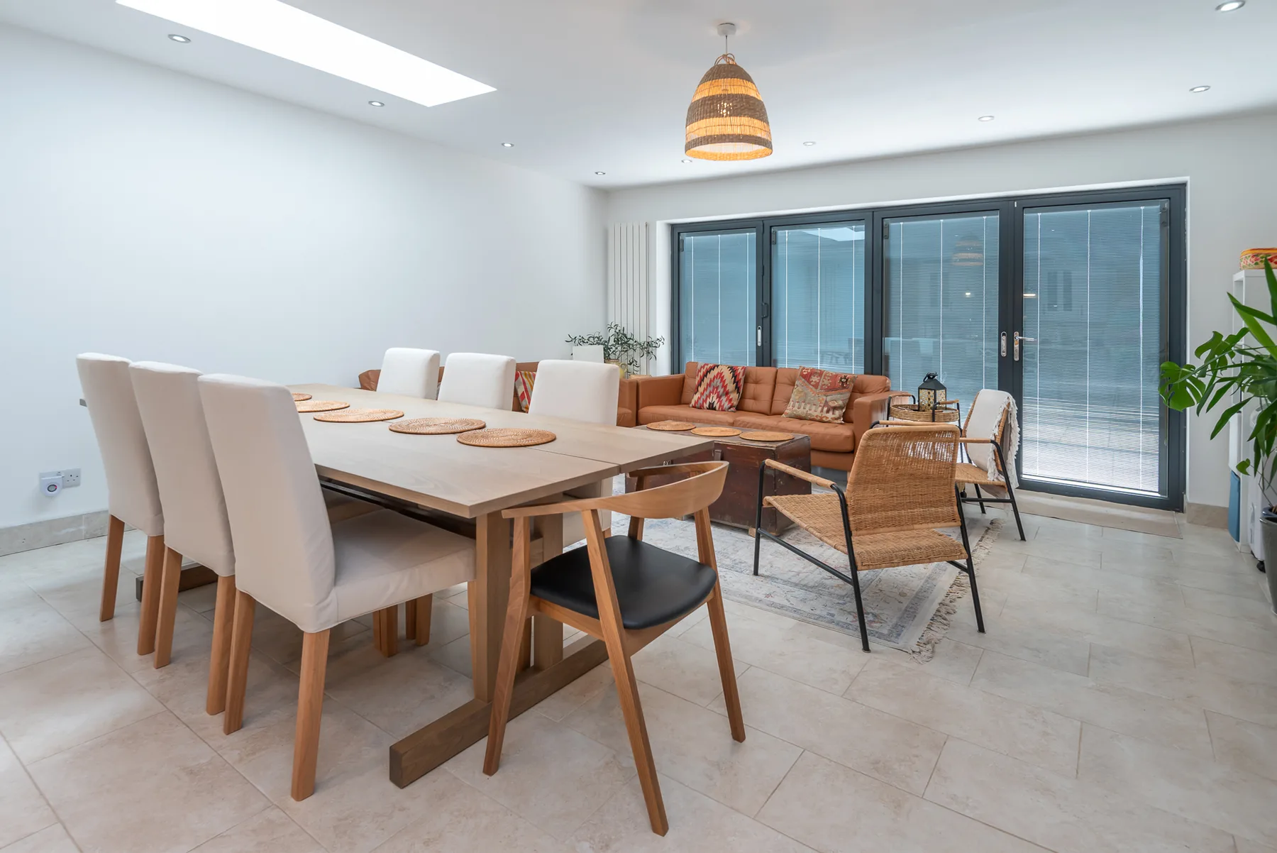 A dining and sitting area with a long table, chairs, and glass doors.