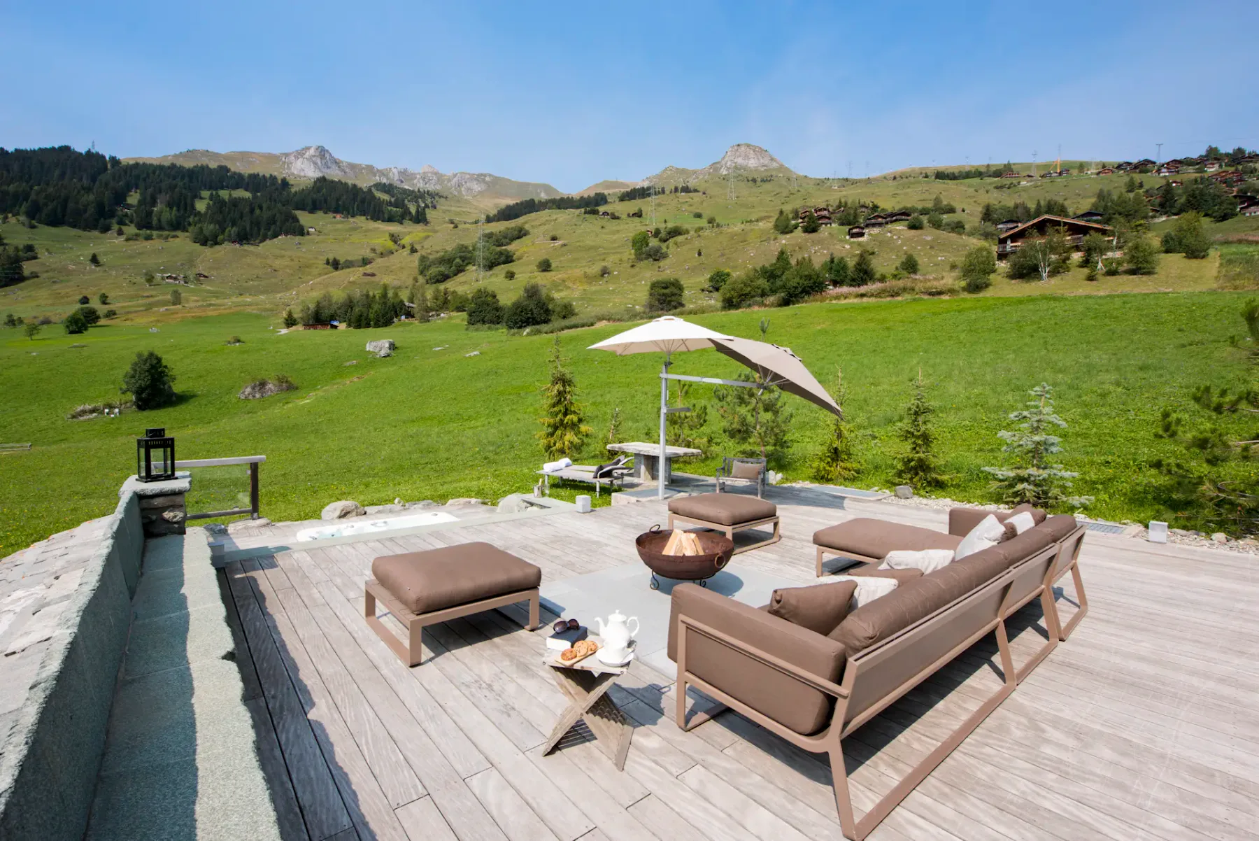Bañera de hidromasaje al aire libre en una terraza de madera con montañas visibles al fondo.